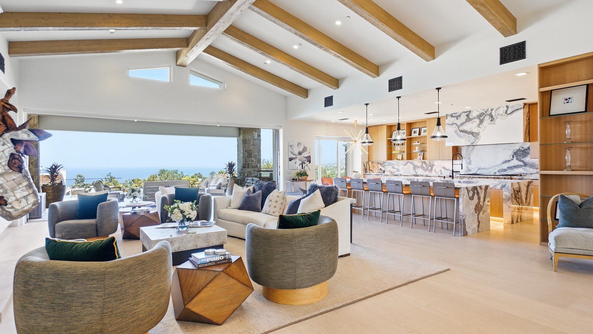 The great room, with beamed ceilings and a wall of glass open to the terrace and ocean.