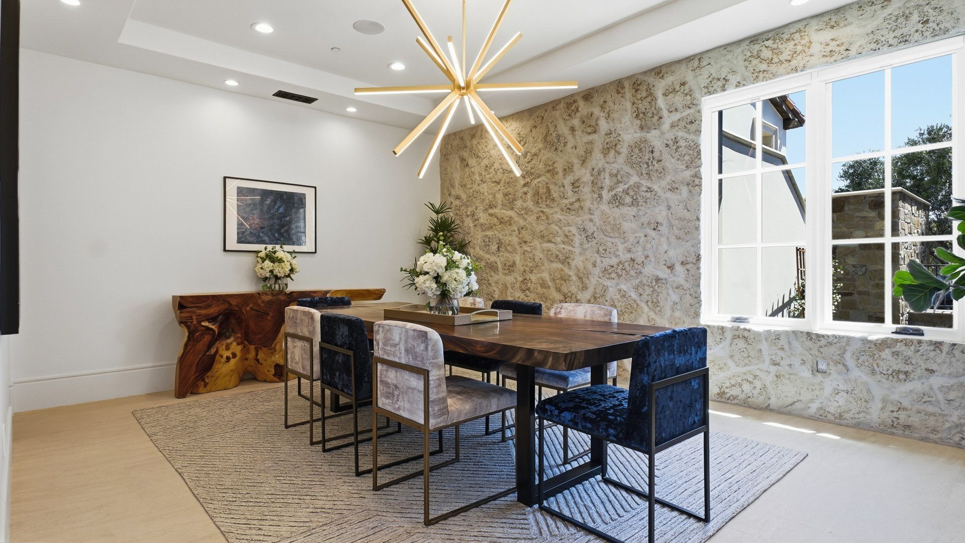 The dining room with a stone wall, a walnut table and a brass chandelier.