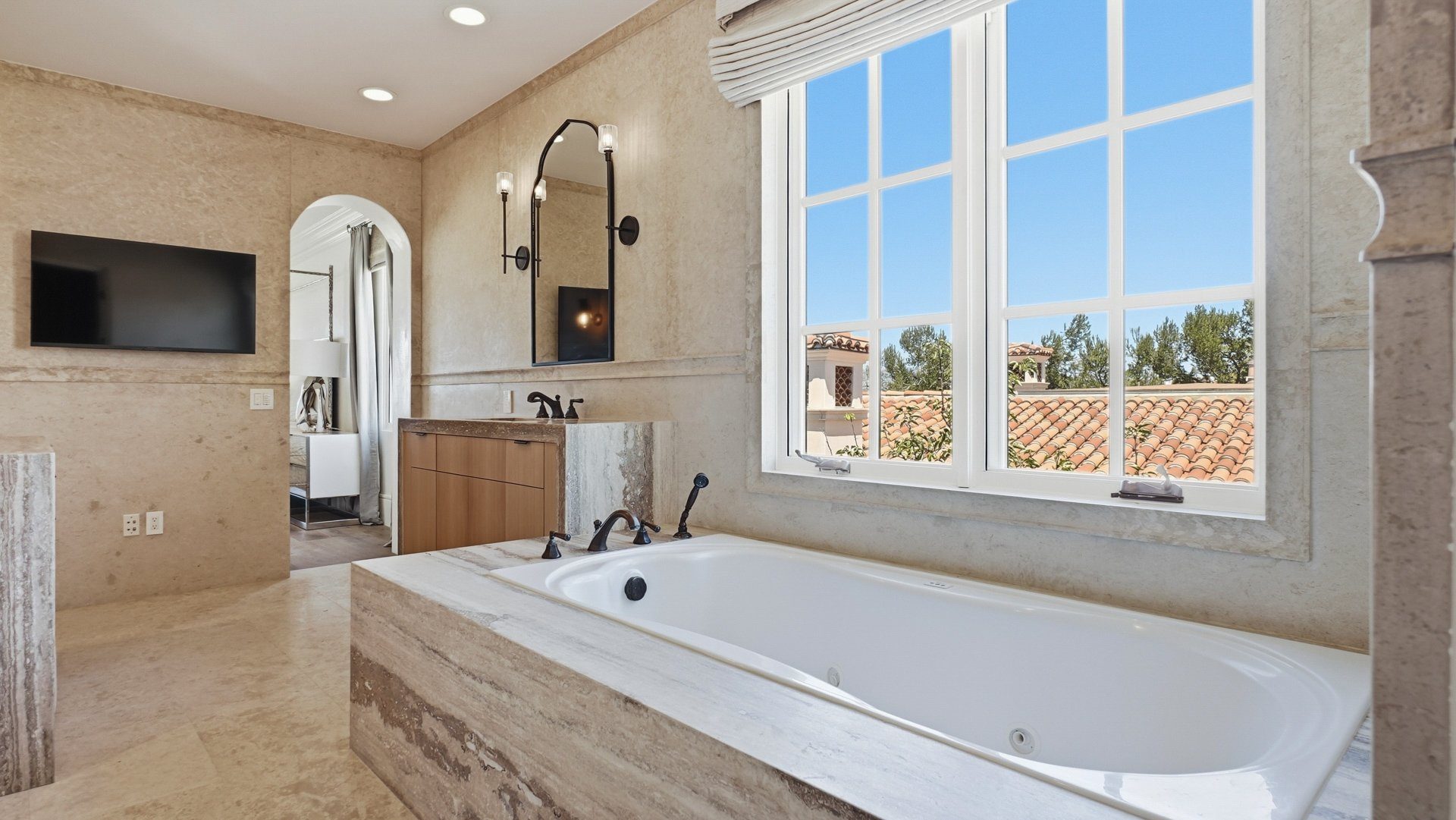 The soaking tub in Ocean Silver travertine, set beneath a window.